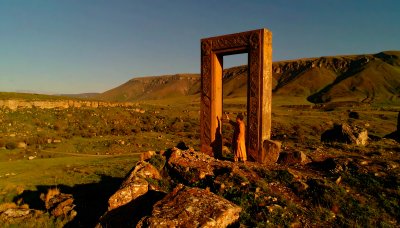 Figure in orange robe by ancient stone doorway in vast landscape