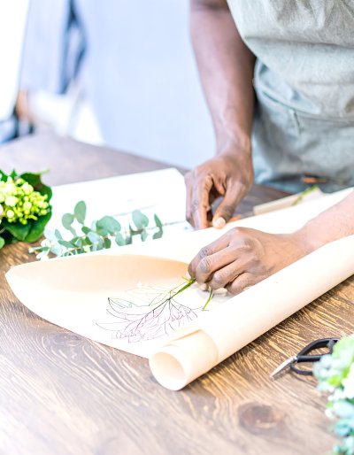 Hands arranging flowers on parchment with plant sketch.