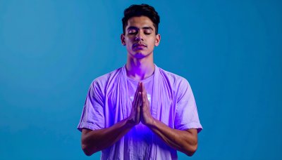 Calm young man meditating with hands together, bathed in purple light