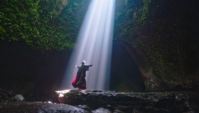 Woman in red robe in cave bathed in light, embracing nature