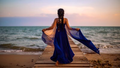Woman in blue dress on pier at sunset, embracing coastal magic