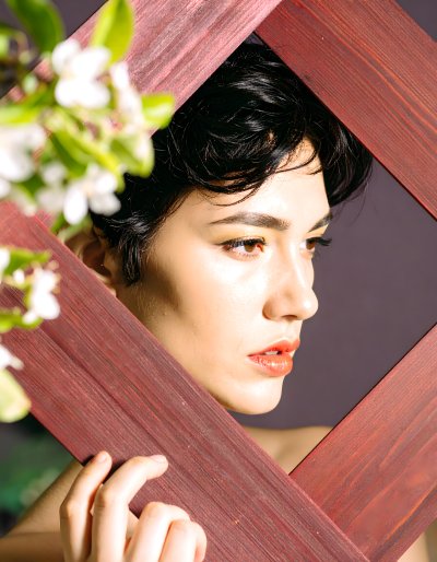 Young woman framed by wood and blossoms, contemplative mood.