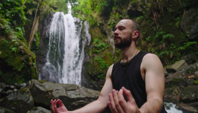 Man meditating by waterfall in lush green nature, finding peace.