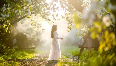 Woman in flowing dress in sunlit forest with blooming trees