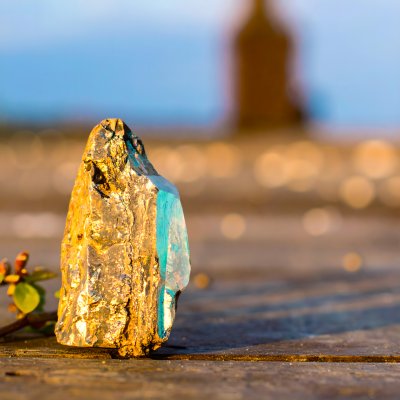 Golden mineral with turquoise, in sunlight on wood