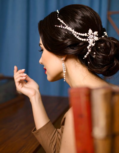 Elegant woman with pearl hairpiece and earrings, blue backdrop.