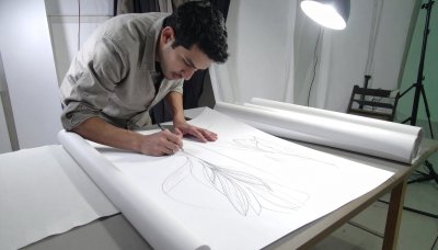 Man sketching delicate floral design on large paper, artistic vision