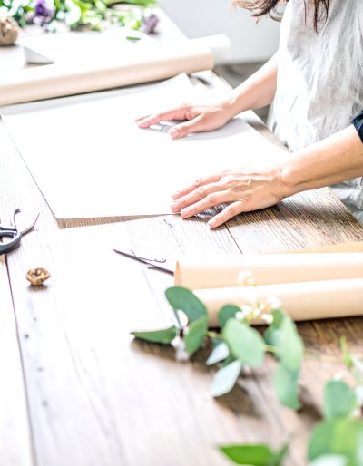 Hands craft floral arrangement with eucalyptus, white blooms on wood
